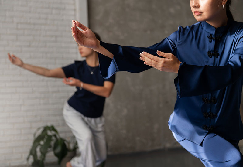 Group of individuals practicing Medical Qigong outdoors, engaged in synchronized movements. They are dressed in comfortable athletic clothing and appear focused and relaxed. The setting includes a peaceful natural environment with greenery, promoting a sense of tranquility and wellness.